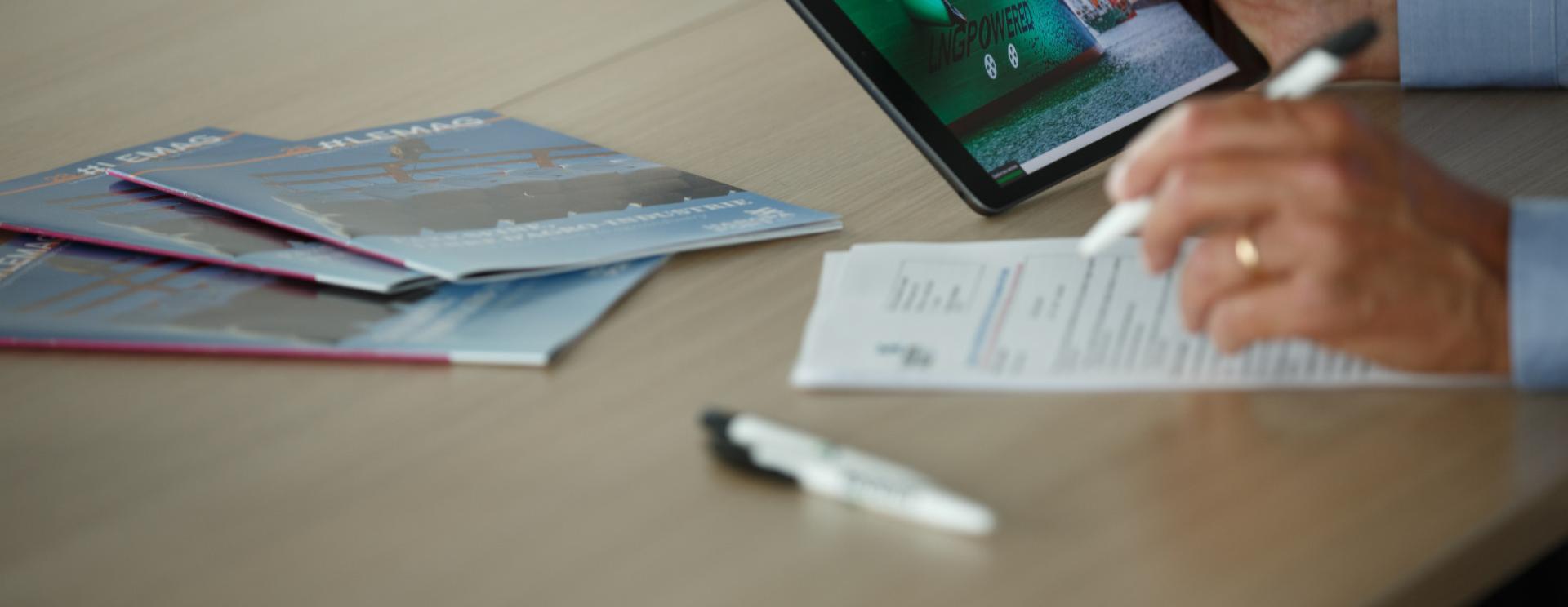 main avec un stylo, l'autre avec une tablette. des magazines HAROPA PORT sur la table