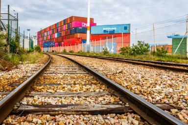 En premier plan, des rails de train. En arrière plan de la photo, des conteneurs ONE, Nile Dutch et autres. - Agrandir l'image, fenêtre modale