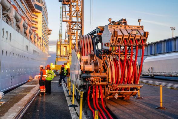 Groupe de personnes opérant le branchement électrique du navire MSC Poesia au quai Pierre Callet du Havre grâce à l'utilisation d'un véhicule équipé de bras articulés et de câbles. - Enlarge image, modal window
